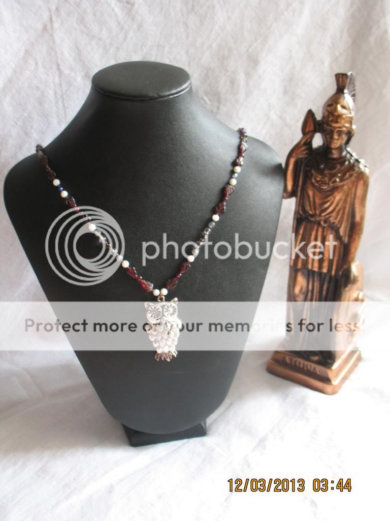 The same necklace as above, but on a black neck form, next to a bronze statue of Athena