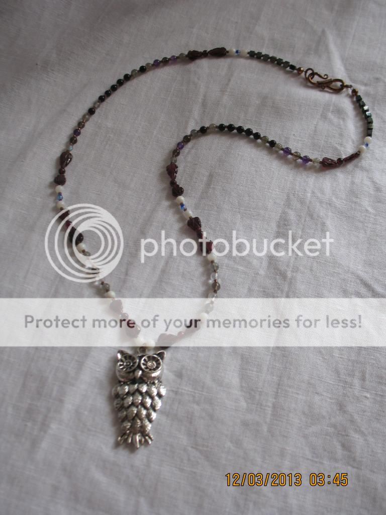 A longer necklace, maybe 22" in length, with a metal owl pendant, and mother of pearl rounds, clear and smokey quartz rounds, garnet rounds, amethyst rounds, obsidian rounds, hematite cubes, garnet leaves, jet rounds, Swarovsky fire-cut Czech glass oblong, and Delica glass seed bead spacers making up the cord.